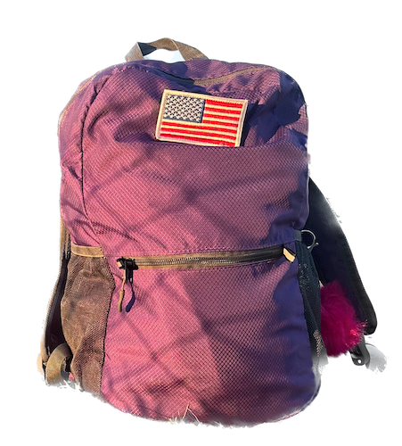 stuffed, zipped purple backpack with American flag patch and pink fuzzy pom attached to side